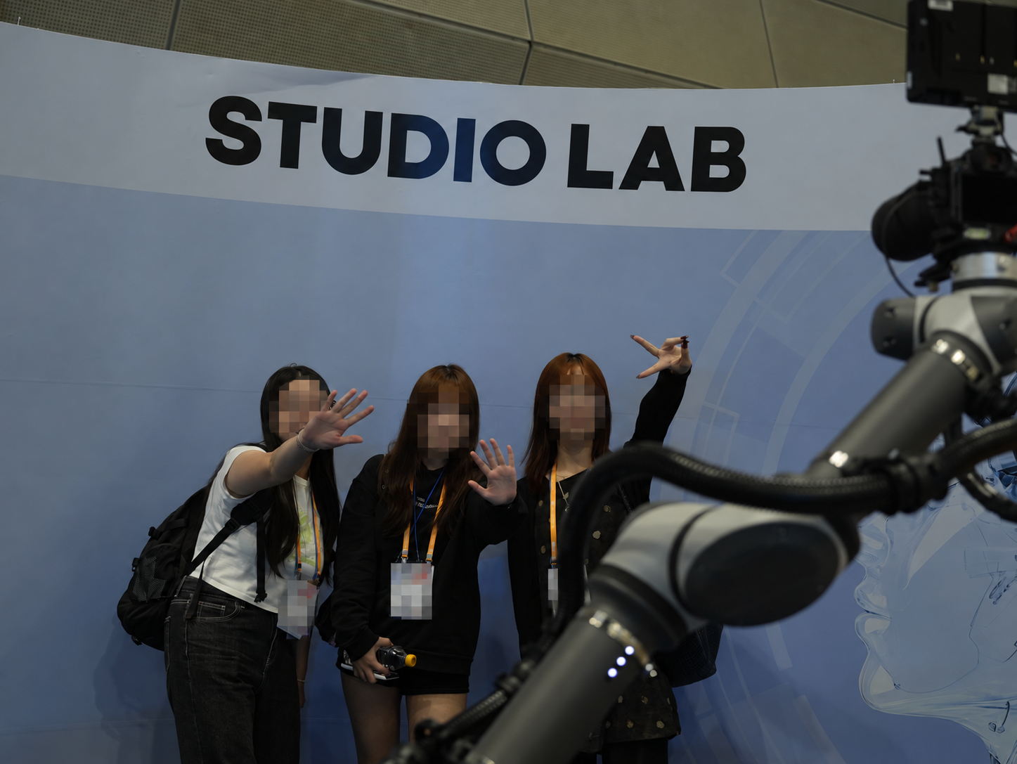 同学们在 STUDIO LAB 展台的拍照机械臂前合影，脸部和胸牌已打码。