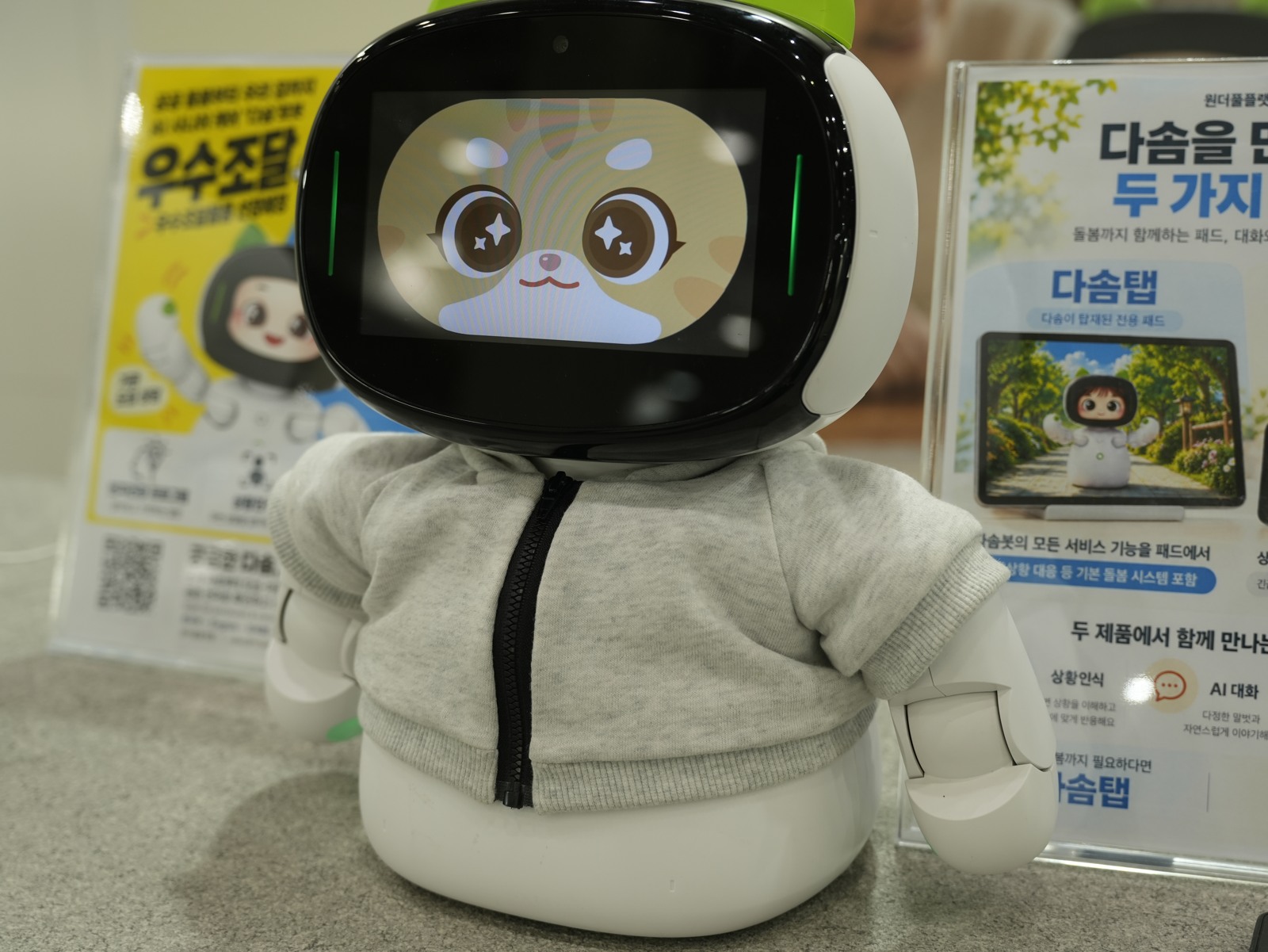 穿着灰色小衣服的 Dasom 陪伴机器人，屏幕上是一张猫脸。